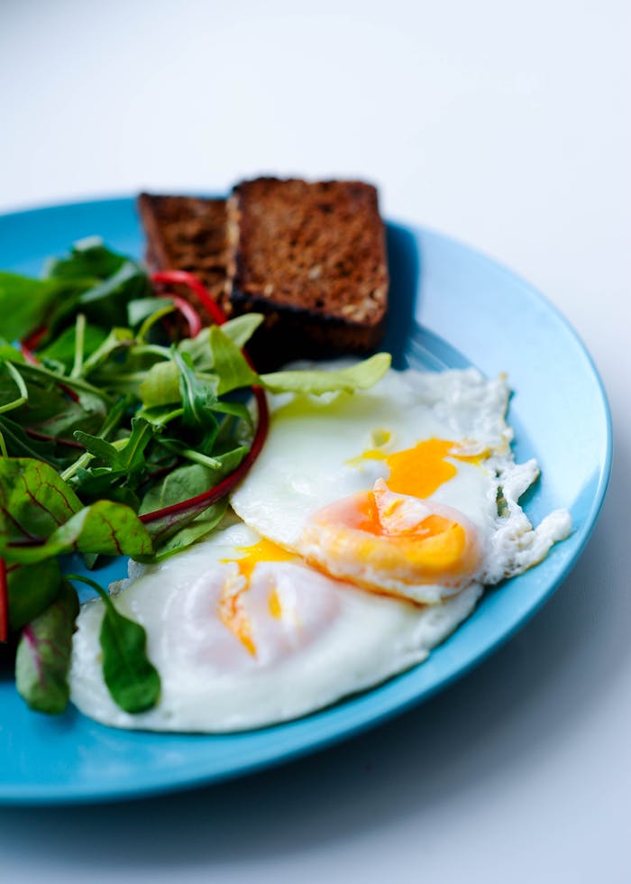 A nutritious breakfast featuring fried eggs, fresh salad, and toasted bread on a blue plate.