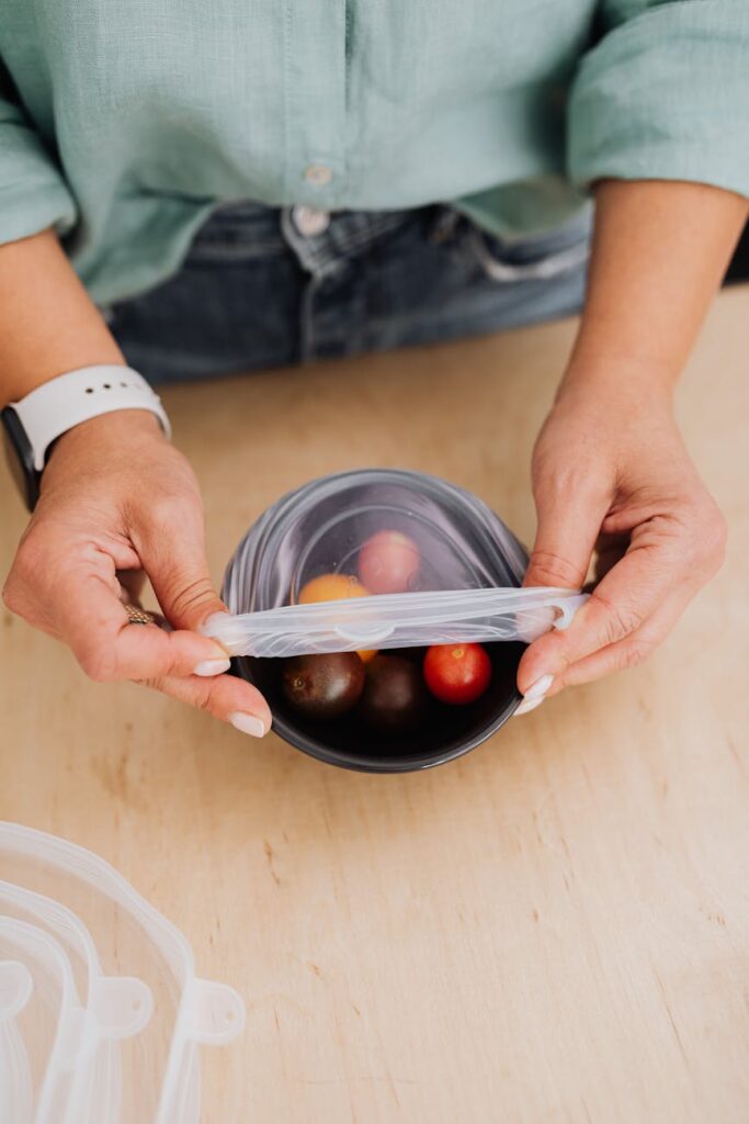Hands placing lid on lunchbox filled with cherry tomatoes on a wooden table.