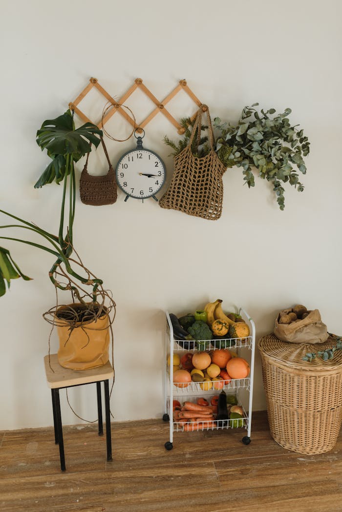 A cozy kitchen nook featuring a wicker basket, hanging bags, lush plants, and fresh fruits on a rack.