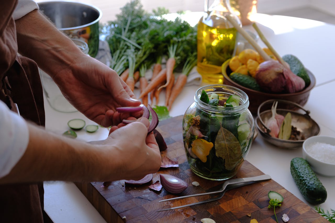Close-up of hands preparing pickled vegetables in a jar with fresh carrots and cucumbers.